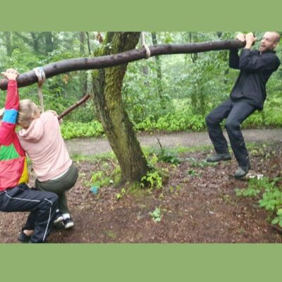 zwei Kinder und ein Erwachsener hängen an Baumstamm